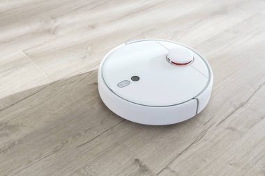 Plastik zeminde beyaz robot elektrikli süpürge. Modern akıllı aygıt temizleme tabanı.