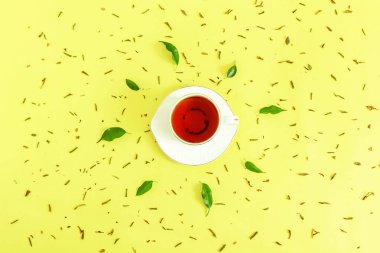 Seramik çay, taze yeşil yapraklar ve sarı zemine saçılmış kurutulmuş bitkiler. Sabah çay seremonisi kavramı. Düz kompozisyon. Yaratıcı yerleşim.