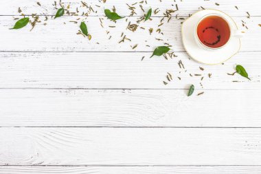 Seramik çay, taze yeşil yapraklar ve beyaz arka plana saçılmış kurumuş bitkiler. Sabah çay seremonisi kavramı. Düz kompozisyon. Yaratıcı yerleşim.