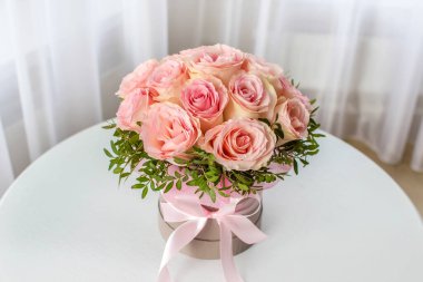 Beyaz bir masada, yuvarlak bir kutuda pembe güllerin güzel bir buketi. Tatil hediyesi, doğum günü, düğün, anneler günü, sevgililer günü, kadınlar günü. Şapka kutusunda çiçekler.