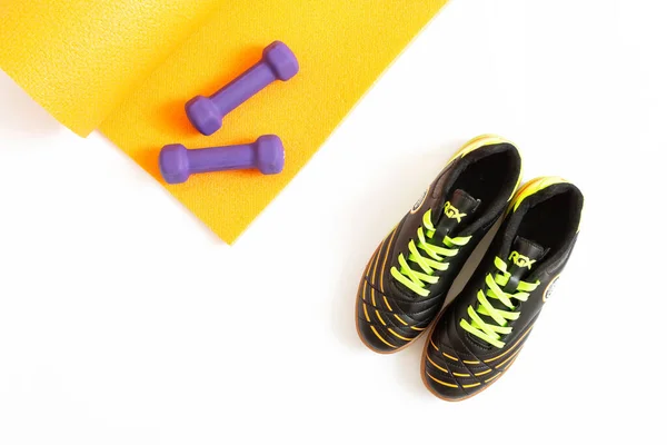 Spor ayakkabıları, dambıllar ve turuncu spor paspası beyaz arka planda izole edilmiş. Düz kompozisyon. Spor anlayışı, spor anlayışı, sağlıklı yaşam tarzı. Üst görünüm.