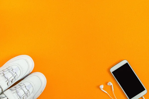 Spor ayakkabılar, kulaklıklı akıllı telefon turuncu fitness paspasının arka planı. Düz kompozisyon. Spor anlayışı, spor anlayışı, sağlıklı yaşam tarzı. Üst Manzara. Boşluğu kopyala.