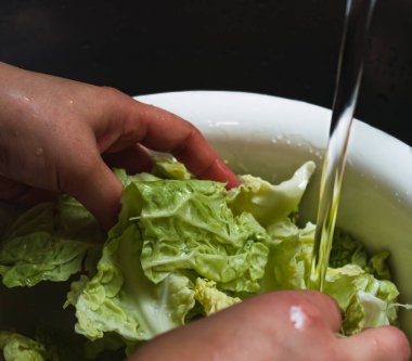 Ev lavabosunda beyaz bir süzgeçle lahana temizleyen eller..