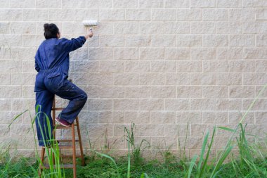 Duvarı eski ahşap bir merdivenin üstünde boya rulosuyla boyayan kadın ressam.