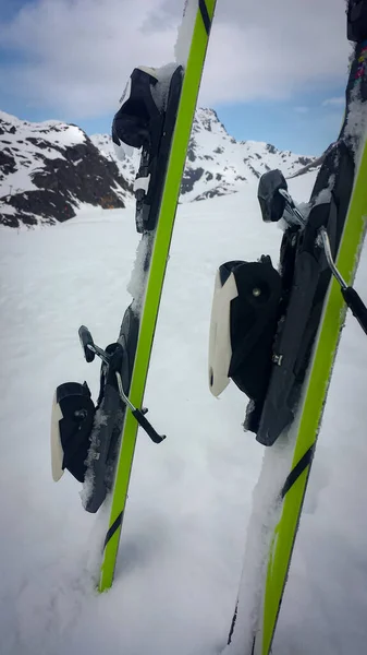 green and black skis nailed to the mountain with white snow