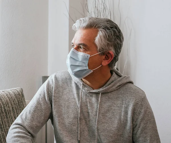Older white-haired man wearing a mask against Coronavirus, Covid - 19 or any other disease, at home