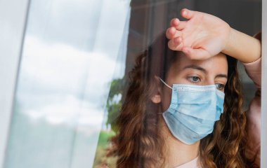 Coronavirus. Koronavirüsü olan genç bir kadın, evde izole edilmiş bir şekilde pencereden dışarı bakıyor ve bir maske ile korunuyor. Salgın