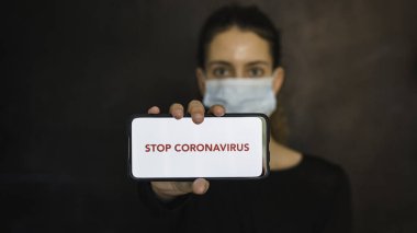 Koronavirüsü durdurun. Coronavirus koruma maskesi takan genç bir kadının elleri cep telefonu ve boş bir ekranla mesaj ya da reklam içeriği yayınlıyor. Sosyal mesafe. Coronavirus cihazları. Sosyal uzaklık. Pandaya karşı koruma