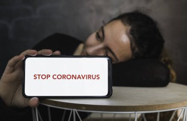Coronavirus 'u durdurun. Genç bir kadın, elinde boş bir ekranla cep telefonu tutarak eski model bir arka plan odasına mesaj veya reklam içeriği koyarak dinleniyor. Sosyal mesafe. Coronavirus cihazları. Sosyal uzaklık. Salgınlara karşı koruma