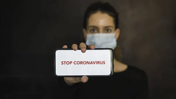 Koronavirüsü durdurun. Coronavirus koruma maskesi takan genç bir kadının elleri cep telefonu ve boş bir ekranla mesaj ya da reklam içeriği yayınlıyor. Sosyal mesafe. Coronavirus cihazları. Sosyal uzaklık. Pandaya karşı koruma