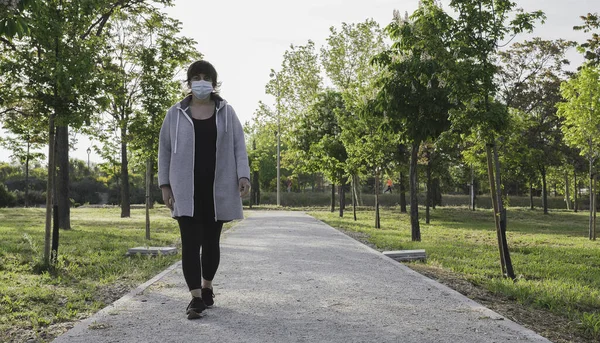 Parkta yürüyen bekar bir kadın, koronavirüs yüzünden sosyal mesafeyi koronavirüs altında tutuyor. Coronavirus cihazları. Sosyal uzaklık. Salgınlara karşı koruma