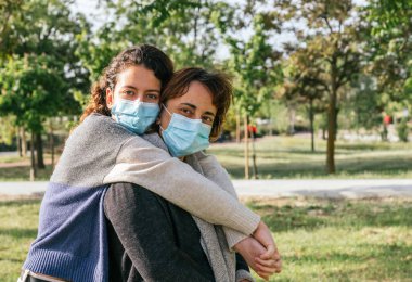 Sosyal mesafe. Koruyucu maskeli bir anne ve kızı parkta sarılıyorlar. Coronavirus salgınını sona erdiriyorum. Coronavirus cihazları. Sosyal uzaklık. Salgınlara karşı koruma