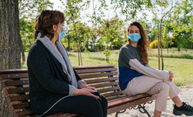 Sosyal mesafe. Anne ve kızı sosyal uzaklıktalar, parkta bankta oturuyorlar. Salgın. Coronavirüs