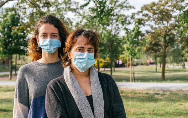Sosyal mesafe. Koruyucu maskeli bir anne ve kızı parkta sarılıyorlar. Coronavirus salgınını sona erdiriyorum. Coronavirus cihazları. Sosyal uzaklık. Salgınlara karşı koruma