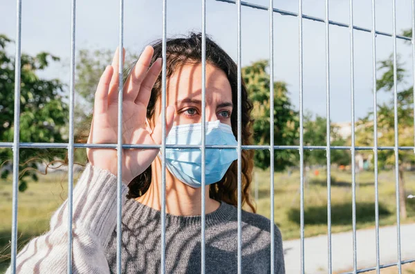 Sosyal mesafe. Maskeli üzgün bir genç bariyerlerin arasından bakıyor. Güvenli mesafeyi koruyoruz. Coronavirus cihazları. Sosyal uzaklık. Salgınlara karşı koruma.