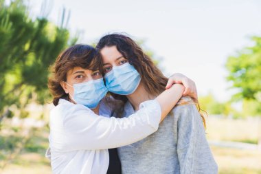 Sosyal mesafe. Parkta sarılmış koruyucu maskeli bir anne ve kız. Coronavirus salgınını sona erdiriyorum. Coronavirus cihazları. Sosyal uzaklık. Salgına karşı koruma. Salgının sonu