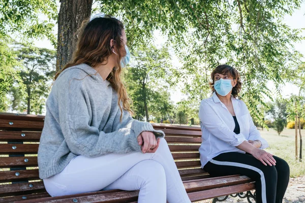 Social distance. Mother and daughter in social distance sitting on a park bench. Pandemic. Coronavirus. Maintaining safe distance sitting on a park bench. Safety distance.