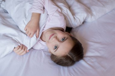 Yatakta tatlı küçük bir kız sabah uyanır ve gülümser. Çocuk yalan söylüyor ve kameraya bakıyor. Karantina sırasında evde vakit geçirmek. Ev konforu.