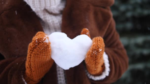 Manos femeninas en manoplas de punto que sostienen el corazón de la nieve en invierno al aire libre . — Vídeo de stock