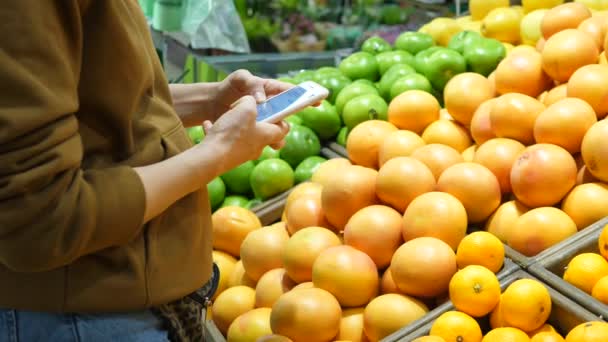 스마트폰을 사용하여 슈퍼마켓에서 쇼핑을 하고 있는 알아볼 수없는 여성 — 비디오