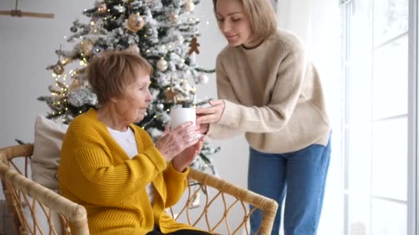 Filha cuidando da mãe mais velha no Natal dando sua xícara de chá . — Vídeo de Stock