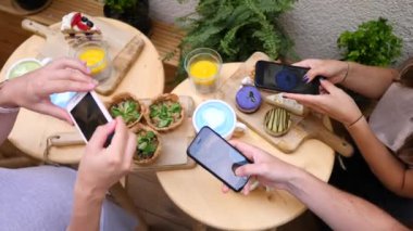 Kahvaltı yaparken akıllı telefonlar kullanarak fotoğraf çeken bir grup arkadaş..