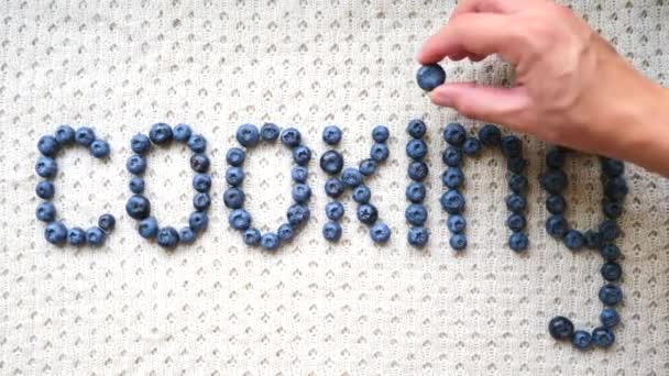 Female Hand Writing A Word "Cooking" From Blueberries. Top View. — Stock Video