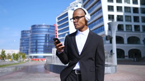 Empresario alegre usando Smartphone, usando auriculares inalámbricos y bailando al aire libre . — Vídeos de Stock