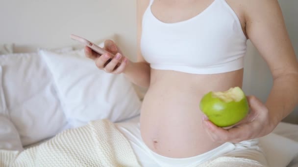 Close-up van zwangere vrouw met behulp van Smartphone en het eten van groene appel. — Stockvideo