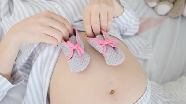 Беременная женщина держит сапоги для своего будущего ребенка — стоковое видео
