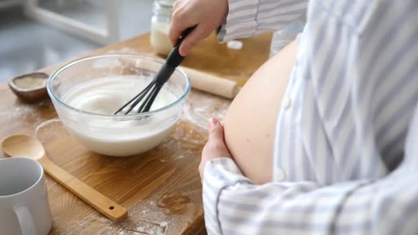 Primer plano de la mujer embarazada batiendo leche en el tazón mientras hornea en la cocina — Vídeo de stock