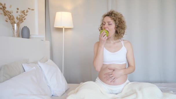 Gesunde schwangere Frau isst grünen Apfel im Bett — Stockvideo