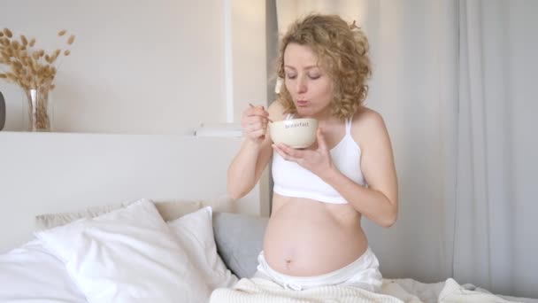 Divertida mujer embarazada hambrienta comiendo cereales para el desayuno en la cama. Concepto de antojos de embarazo . — Vídeos de Stock