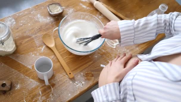 Primer plano de la mujer embarazada golpeando la leche en un tazón mientras cocina el desayuno en la cocina . — Vídeos de Stock