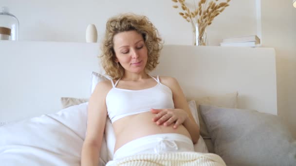 Молода вагітна жінка сидить на ліжку — стокове відео