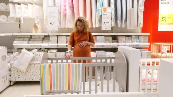 Jonge zwangere vrouw kiezen voor kinderbedje of babybedje in de meubelwinkel. — Stockvideo