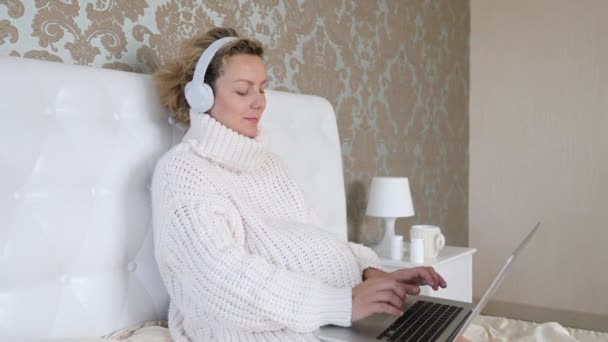 Fiatal terhes nő használja Laptop viselő fejhallgató az ágyban. — Stock videók