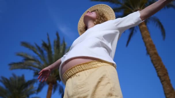 Zwangere vrouw met armen uitgestrekt tegen de blauwe lucht op vakantie. — Stockvideo