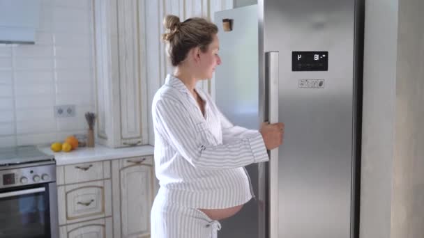 Młoda kobieta w ciąży szuka w lodówce na coś do jedzenia. — Wideo stockowe