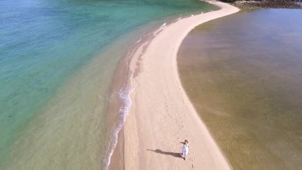 Воздушный: женщина в белом платье прогуливается по белому пляжу . — стоковое видео