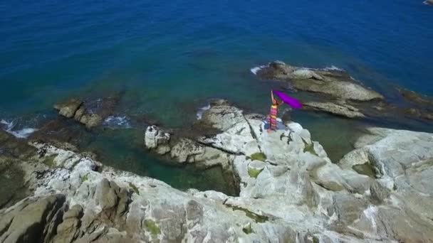 女人穿着五颜六色的衣服站在岩石上看着大海。 空中业务. — 图库视频影像