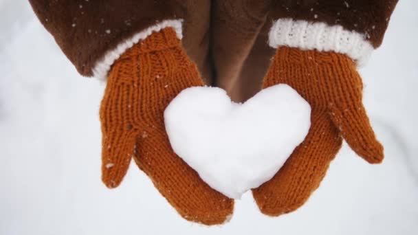 Gros plan de filles mains dans gingembre mitaines tricotées tenant coeur de neige en hiver . — Video