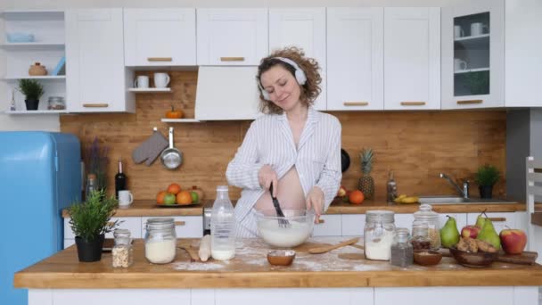 Feliz Conceito de Gravidez Saudável. Mulher grávida em fones de ouvido dançando e cozinhando na cozinha . — Vídeo de Stock