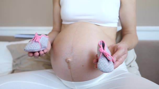 Closeup de mulher grávida segurando botas para seu futuro bebê perto de sua barriga — Vídeo de Stock