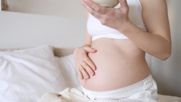 妊娠中の女性はベッドで朝食を取りながら彼女の腹に触れる. — ストック動画