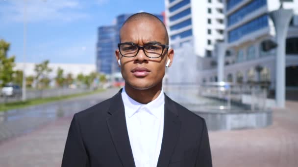 Jóképű fiatal üzletember szemüveget és vezeték nélküli Bluetooth fülhallgatót visel. — Stock videók