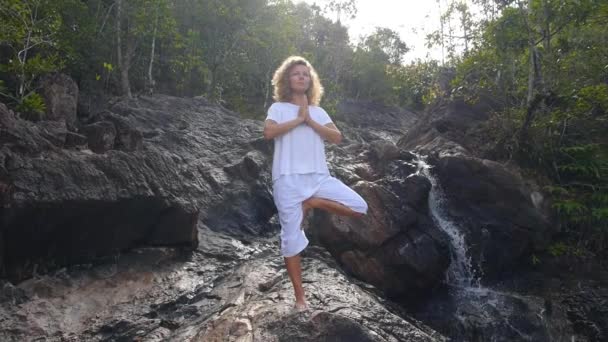 Ung kvinna gör yoga vid vattenfall i vita kläder — Stockvideo
