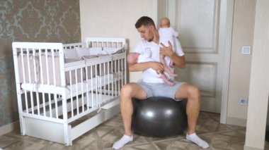 Mutlu genç baba, ikiz bebekleri kollarında, yatak odasında spor salonunda emziriyor..