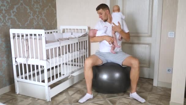 Feliz padre joven amamantando bebés gemelos en sus brazos en el dormitorio en Fitball . — Vídeo de stock