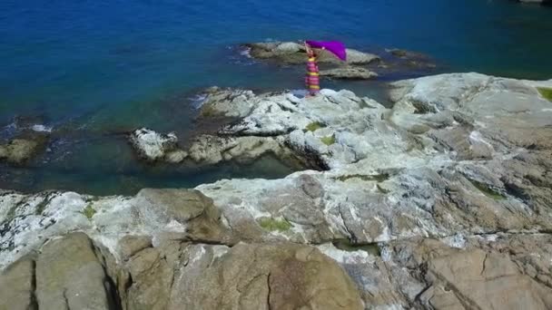 Mujer joven en vestido de color en las rocas junto al mar. Tiro aéreo . — Vídeos de Stock